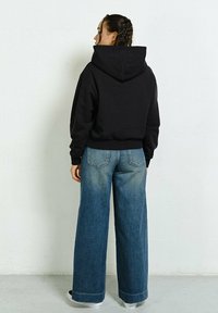Czarna, luźna bluza z kapturem, zestawiona z jasnoniebieskimi, szerokimi dżinsami. Gładka tekstura i kontrastowy kolor denimu z wyblakłym wykończeniem.
