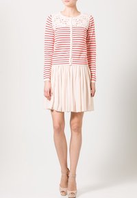 Randig röd och vit långärmad cardigan med spetsdetalj på axlarna, ihop med en krämfärgad, veckad klänning och beige klackar.