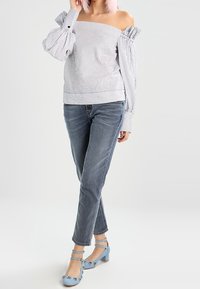 Blusa a rayas sin hombros con mangas abullonadas, combinada con jeans de un azul claro y tacones azules con correas adornadas con acentos florales.