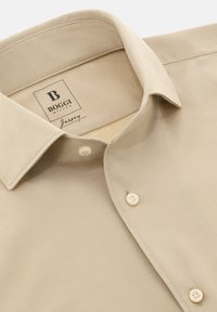 Camicia in jersey beige con colletto classico, due bottoni bianchi e una texture intrecciata. L'etichetta riporta "Boggi Milano Jersey."