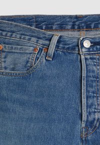 Blue denim jeans with a zipper fly, copper hardware, and orange stitching. Features a classic five-pocket design and a solid texture.
