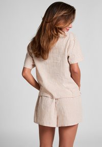 Beige en witte geblokte top met korte mouwen en bijpassende shorts, gemaakt van lichte stof. De set heeft een losse fit en subtiele textuur.