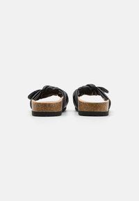 Svart skinnsandal med vridd stroppdesign, korkfotbed og teksturert svart såle. Minimalistisk og åpen bakstil.