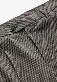 Braun und marineblaue Karohose mit Knopfverschluss, flachem Frontdesign und Seitentaschen; der Stoff hat eine glatte Textur mit leichtem Webmuster.