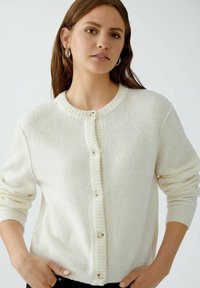 Weißer Strickcardigan mit runder Ausschnitt, gerippter Knopfleiste, langen Ärmeln und strukturierter Stoff. Verfügt über fünf Knöpfe und Detail an den Bündchen.