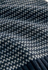 Tekstureret uldsjaal med et m�ørkeblåt og cremefarvet houndstooth-mønster, med en blød, fuzzy overflade og frynser i kanterne.