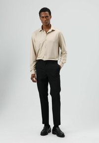 Beige shirt met lange mouwen, zwarte getailleerde broek en zwarte loafers. Gladde stof met knoopdetails. Strak ontwerp, aansluitende pasvorm.