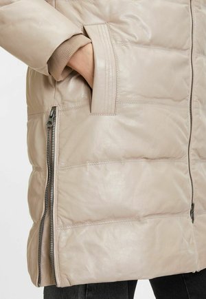 Giacca imbottita in pelle beige chiaro con una texture lucida, dotata di cerniera laterale e polsini in maglia. Dettagli includono cuciture orizzontali e tasche.