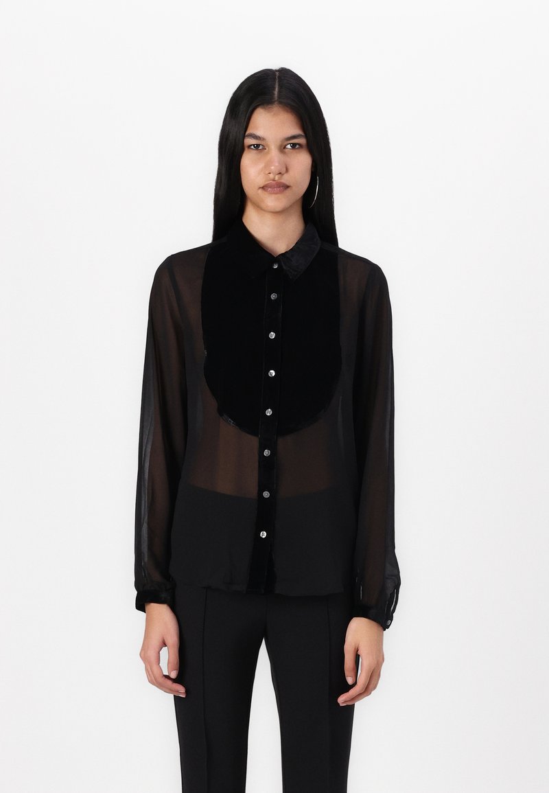 Blusa preta transparente com colarinho de veludo, apresentando fechamento frontal com botões e mangas longas com punhos botão. Cor preta sólida em toda a peça.