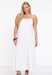Weißes Maxikleid mit einem gestuften Rüschensaum, verstellbaren Schulterträgern und einem lockeren Schnitt, aus weichem, leichtem Stoff gefertigt.
