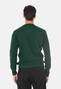 Maglione verde a costine con scollatura a girocollo, maniche lunghe e un design aderente. Realizzato in materiale morbido, abbinato a pantaloni neri.