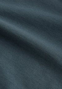 Tmavo zelená textúrovaná látka s hladkým povrchom a jemným vlnkami, zobrazujúca jemne pletený vzor a ľahký, flexibilný materiál.