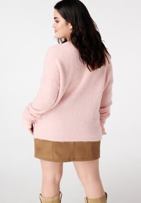 Pull doux rose clair avec épaules tombantes et détails en dentelle aux poignets, associé à une mini-jupe en daim beige.