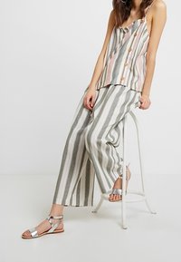 Top sin mangas a rayas con botones en rosa y verde, combinado con pantalones de pierna ancha y cintura alta, y sandalias planas plateadas.