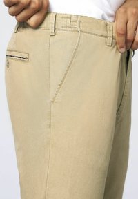 Khaki trousers made of cotton, featuring a textured finish, side pockets, and visible stitching along the seams.