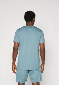 T-shirt de sport bleu clair à manches courtes, texture lisse, encolure arrondie, associé à un short assorti, vu de dos.