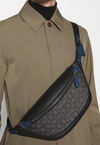Sac à bandoulière avec une base en cuir noir, un tissu à motifs gris, des accents bleus et une fermeture zippée. Dispose d'une sangle réglable pour un confort optimal.