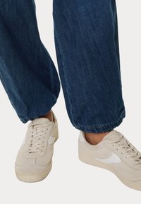 Beige semišové tenisky s bílými akcenty, spárované s tmavěmodrými denimovými kalhotami s elastickými manžetami u kotníků.