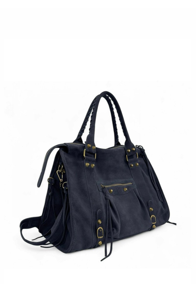 Sac à main en daim bleu marine foncé avec des poignées tressées, une poche zippée à l'avant, des boucles en laiton et des pendantifs décoratifs sur fond blanc.