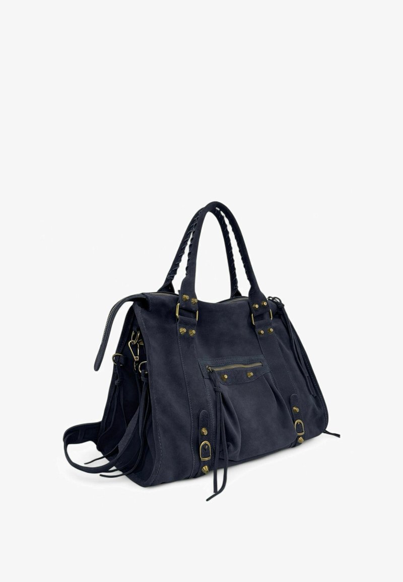 Sac à main en daim bleu marine foncé avec des poignées tressées, une poche zippée à l'avant, des boucles en laiton et des pendantifs décoratifs sur fond blanc.