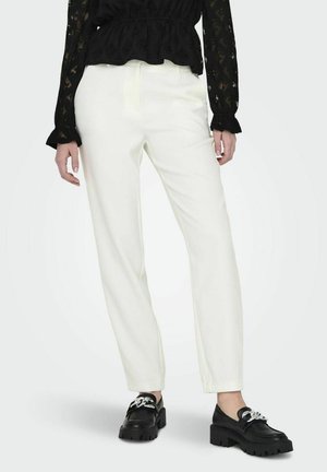 Pantalons blancs ajustés à coupe droite, texture lisse et taille haute, associés à des chaussures noires à semelles épaisses et à quincaillerie en argent.
