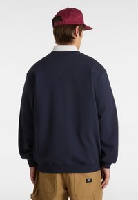 Sudadera de cuello redondo en color navy con un ajuste relajado, puños acanalados, combinada con pantalones cargo color caqui que tienen un parche con logo.
