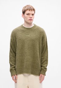 Maglione verde oliva con una superficie testurizzata e pelosa, scollo a girocollo e maniche lunghe; polsini e orlo a coste.