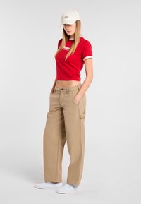 Rode cropped t-shirt met witte rand, khaki wijde broek en witte sneakers. Pet in het wit met klein logo aan de voorkant. Gladde stofstructuren.