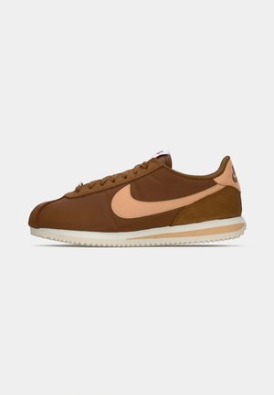Brown athletic shoes with a pink Nike swoosh, featuring a smooth leather upper, suede accents, and a textured rubber sole.