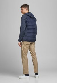 Hooded jacket in navy with a padded back, soft front, and ribbed cuffs, paired with beige pants and white sneakers.