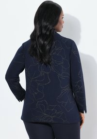 Maglia a maniche lunghe blu navy con motivi floreali metallici, texture liscia e vestibilità rilassata. Progettata con orlo dritto e spacchi sui lati.