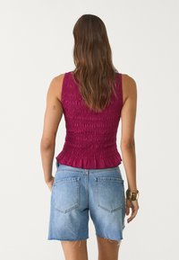 Fuchsia sleeveless top with gathered texture and a peplum hem, paired with light blue denim shorts with frayed edges and back pockets.