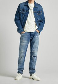 Chaqueta de denim y jeans claros desgastados combinados con una camiseta blanca, junto a zapatillas blancas. Diseño simple, ajuste casual.