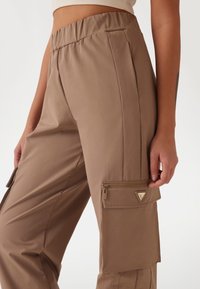 Beige cargobroek met een elastische tailleband, zijzakken en een ritszak op het been met een driehoekige hardware accent.