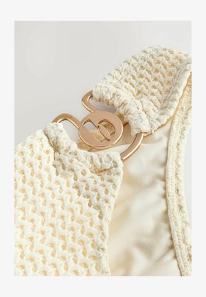 Kudottu kerma väri bikinitoppi, jossa on texturoitu virkkauskuvio, kultaisella varustetulla kiinnityksellä ja sileällä sisävuorella.