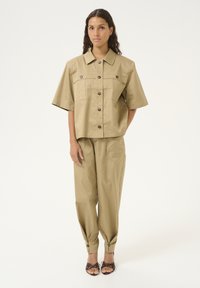 Khaki dvoudílný outfit, skládající se z cropped košile s knoflíky a krátkým rukávem a odpovídajících zúžených kalhot s manžetami. Hladká textura.