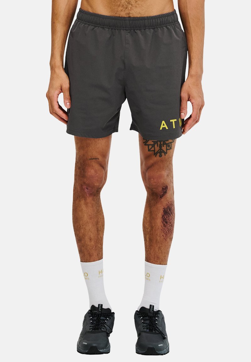 Krótki szary szorty z elastyczną talią i żółtym napisem "ATW" z przodu, zestawione z ciemnymi butami i białymi skarpetami z złotym napisem.