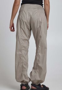 Lätta, beige, byxor med elastisk midja och samlade anklar. Har en texturerad tyg och en liten varumärkesetikett på baksidan.