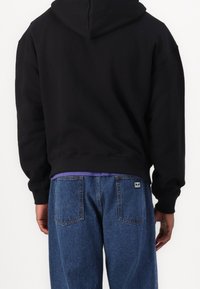 Sweat à capuche noir à coupe courte, ourlet côtelé et manches longues, associé à un jean en denim bleu moyen avec poches arrière.