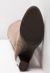 Botín de ante marrón con suela de goma texturizada y tacón moderado. Superficie superior lisa con detalles mínimos de costura.