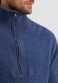 Fleece-Pullover in Dunkelblau mit einem gerippten Stehkragen und einem halben Reißverschluss. Texturiertes Material mit einer weichen Oberfläche und kontrastierender Reißverschluss-Detail.
