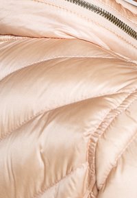 Gros plan d'une veste matelassée rembourrée rose pâle avec des coutures visibles et une fermeture éclair argentée.