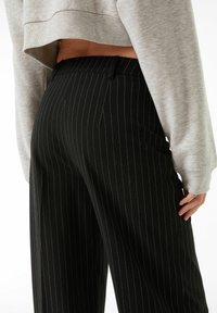 Svarta byxor med smalrandig design och skräddarsydd passform, med hög midja och sidofickor, i kombination med en ljusgrå kort sweatshirt.