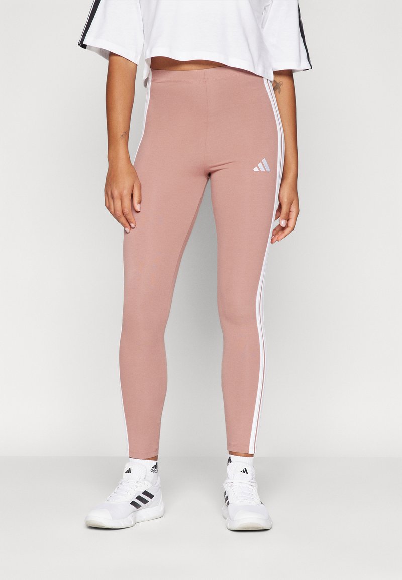 Rosa leggings i stretchmaterial, med vita sidostickningar och Adidas-logotypen på vänster lår. Bärs med en vit kortärmad topp.
