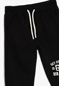 Zwarte joggingbroek van zacht materiaal, met een geribbelde tailleband, witte trekkoord en zijzakken. Inclusief witte bedrukte tekstdetails.