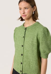 Grøn strikket cardigan med korte pufærmer, rund halsudskæring og mørke knapper. Tekstureret stof med ribbede kanter og manchetter.