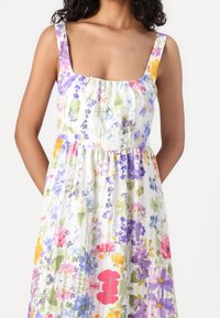 Blommig klänning i lätt material; har en fyrkantig halsringning, breda axelremmar och ett färgglatt tryck med lila, rosa, gula och gröna blommor.