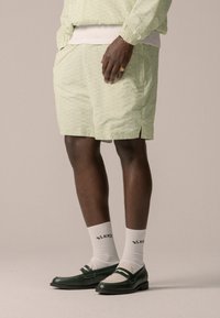 Shorts vert clair avec une texture à motif subtil, associés à des mocassins verts et des chaussettes blanches. Comprend des poches latérales et une coupe décontractée.
