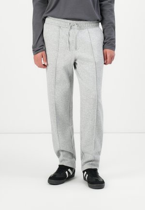 Light grey sweatpants with a drawstring waist, side seam detailing, and a relaxed fit, paired with black sneakers featuring white stripes.