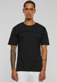 Černé tričko s crew neck výstřihem a krátkými rukávy, s horizontálním panelem přes hrudník. Hladká textura, volný střih, minimalistický design.